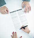 high-angle shot of a young woman signing a divorce decree document in front of a young man