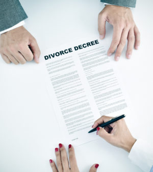 high-angle shot of a young woman signing a divorce decree document in front of a young man